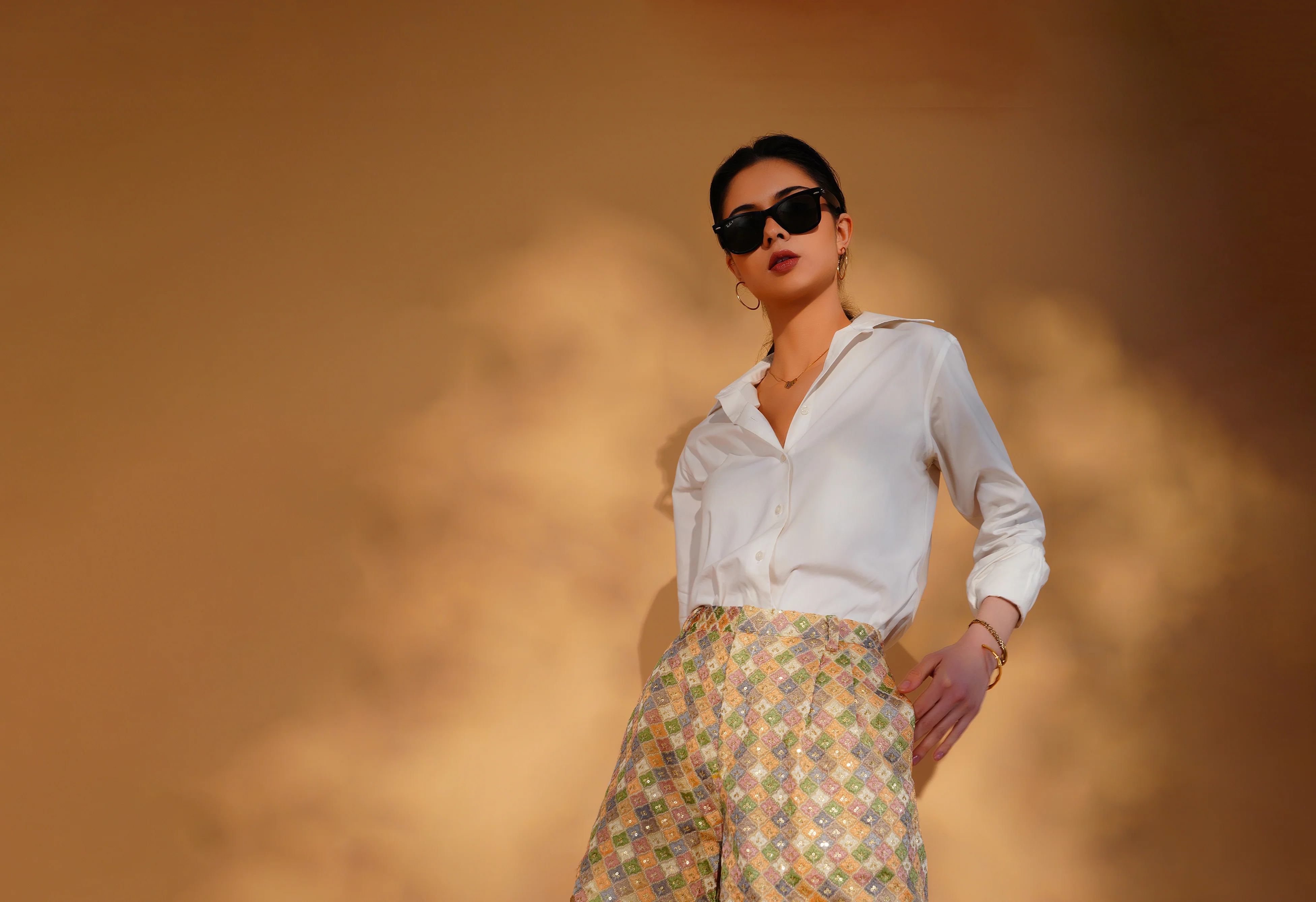 Woman wearing a white shirt and patterned pants against a warm-toned background