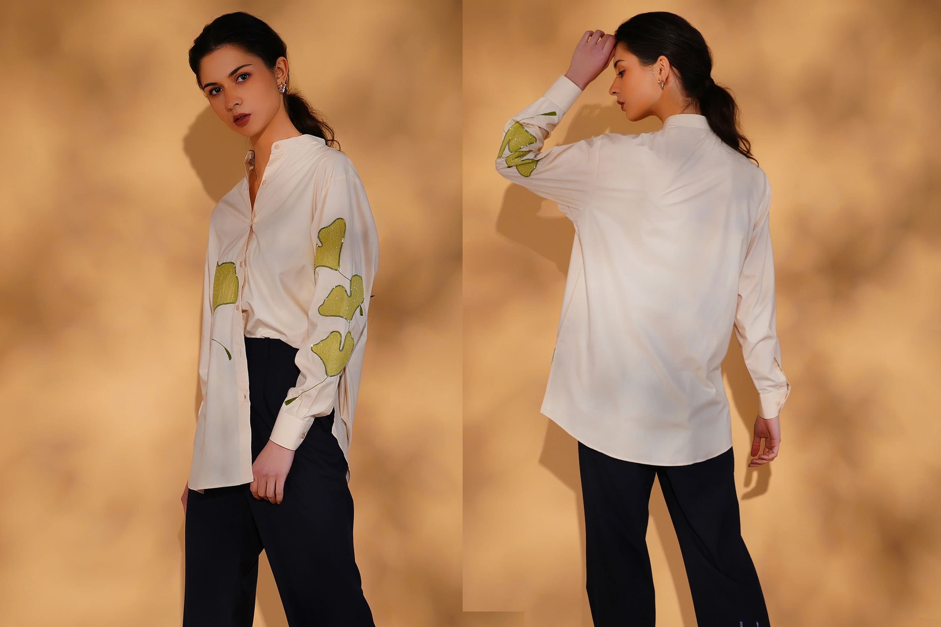Woman wearing a white blouse with green patterns and black pants against a beige background