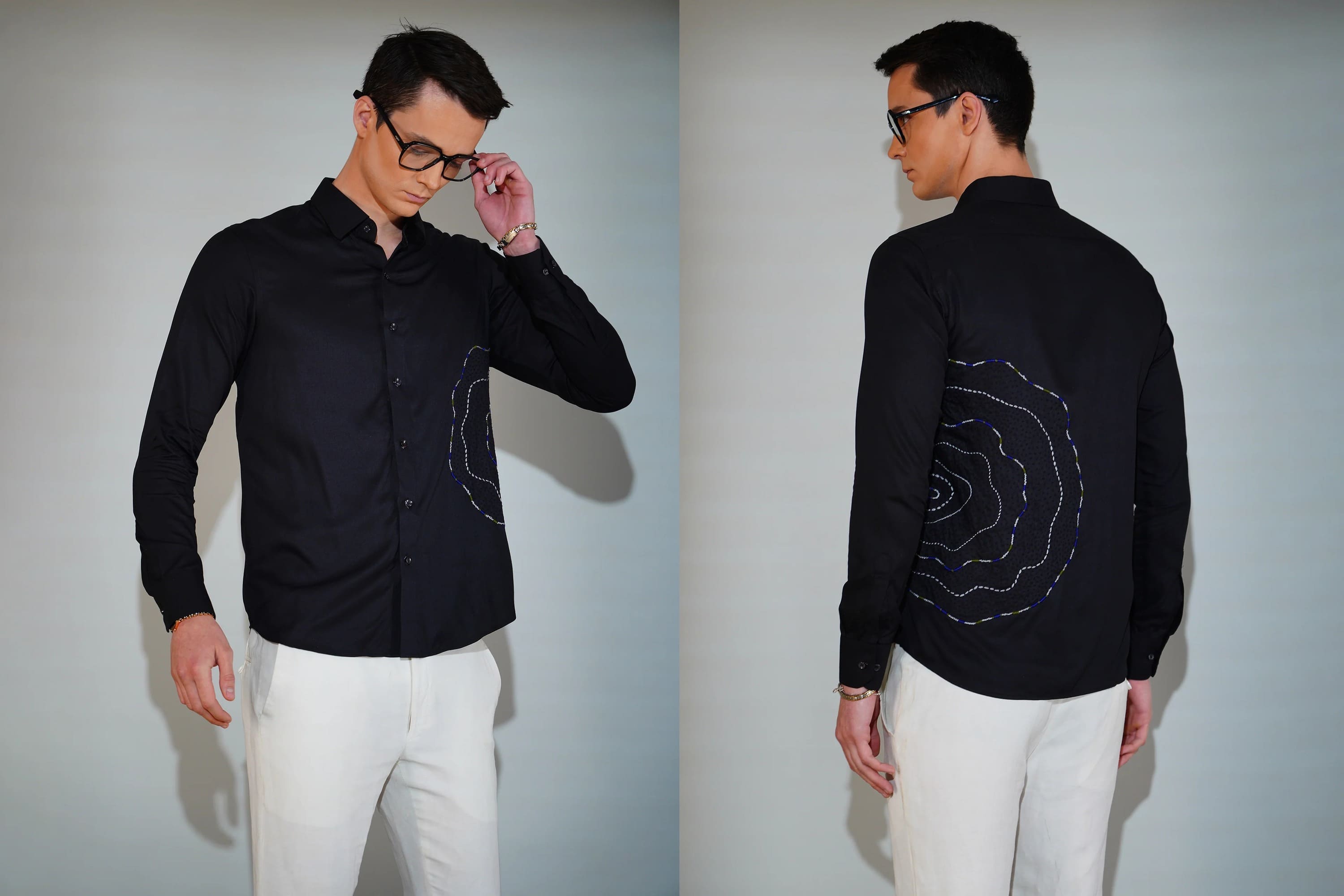 Man wearing a black shirt with white embroidery, standing against a plain background.